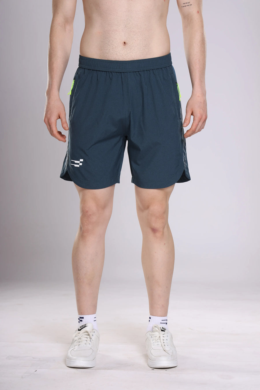 Apex Performance Shorts in dark teal, front view on a model with white logo and lime zip pulls