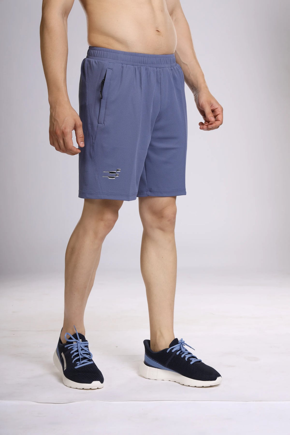 Club Performance Shorts in Dark Fin, angled front view on a model showing the zip pocket and logo
