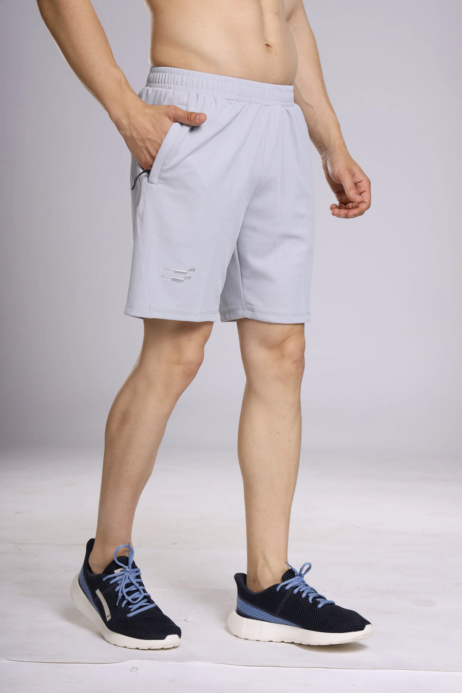 Club Performance Shorts in silver haze, side view on a model with a hand in the side pocket, styled with navy trainers