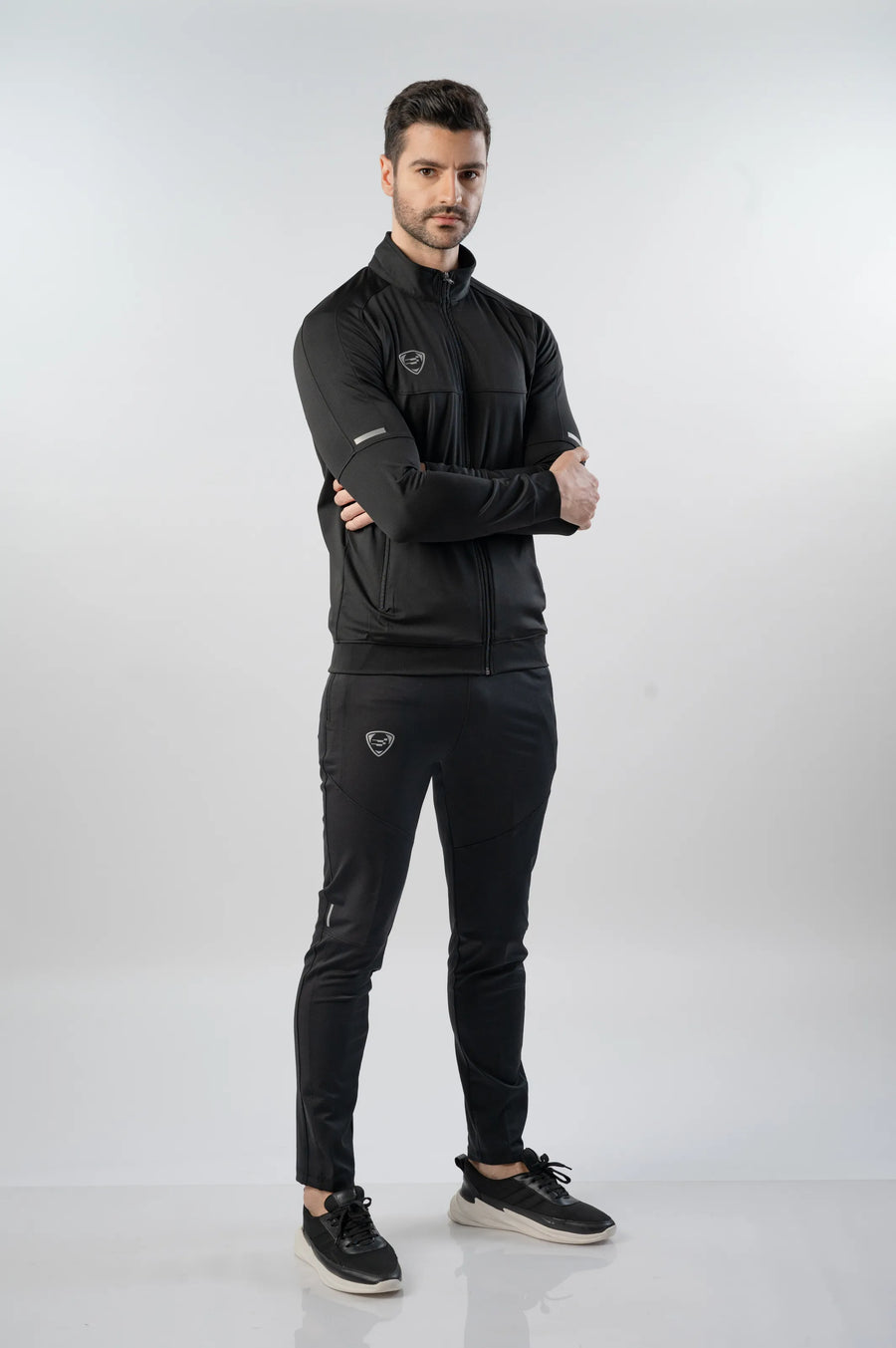 Firebird Signature Track Top in black, full-length front view with arms crossed, worn with black track pants