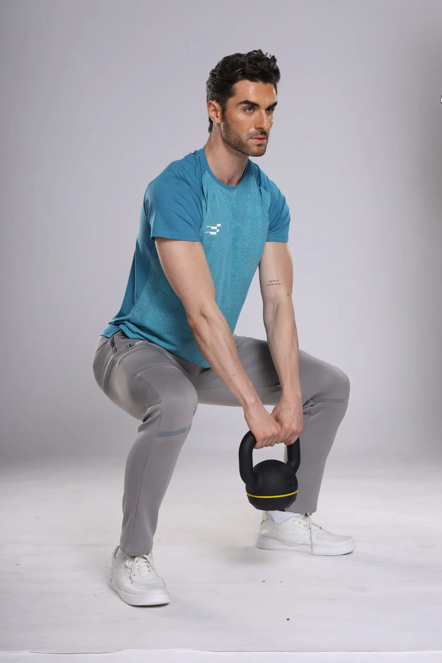 Fit-Gear Octagon T-Shirt in teal, worn by a model doing a kettlebell squat in grey track pants