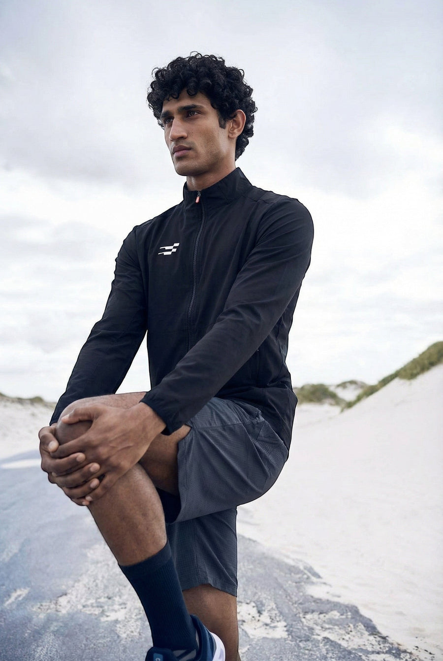 Tech-Shell Performance Track-Top in navy, worn outdoors on a beach with dark shorts during a leg stretch